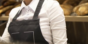Female baker seller working on computer and selling bread in supermarket.